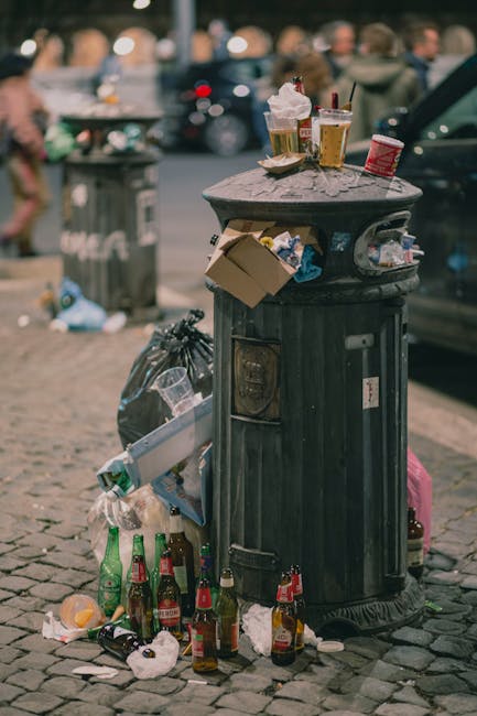A collection of large white plastic rubbish bags tied with orange plastic tie straps, filled with waste material and stacked outdoors on a paved surface. The bags are made of semi-transparent plastic,